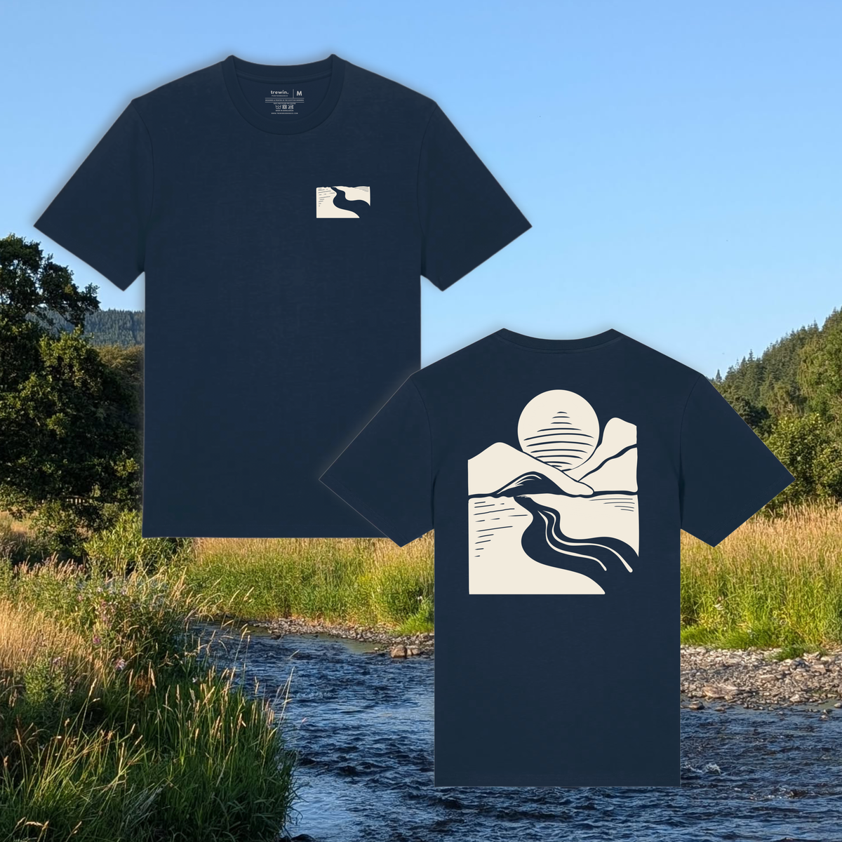 Two navy blue short-sleeve t-shirts shown against an outdoor stream and grassy landscape. The front shirt has a small cream square logo on the left chest, and the back shirt has a large cream graphic of a sun, mountains, and a river.