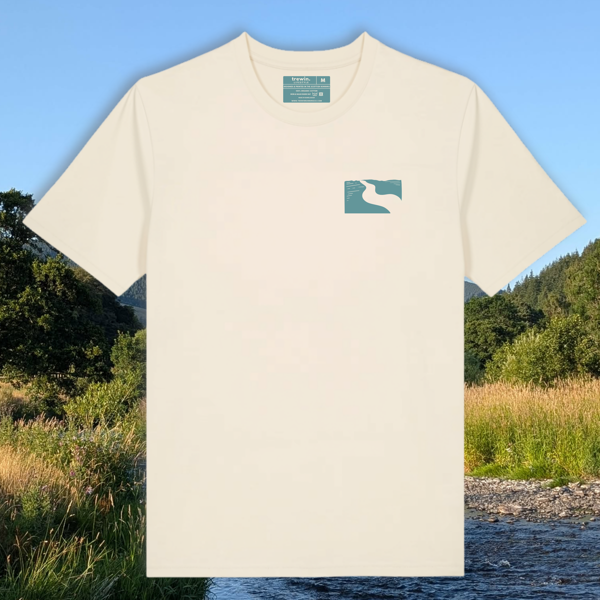 An off-white short-sleeve t-shirt with a small teal and white river banks logo on the left chest, presented against a scenic outdoor background of a river and forest.