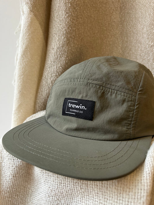 An olive green 5-panel cap with a black 'trewin. running co.